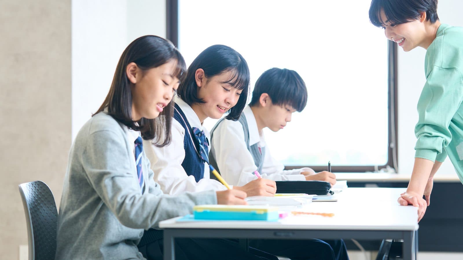 机に並んだ3名の生徒に、講師が横について指導している様子